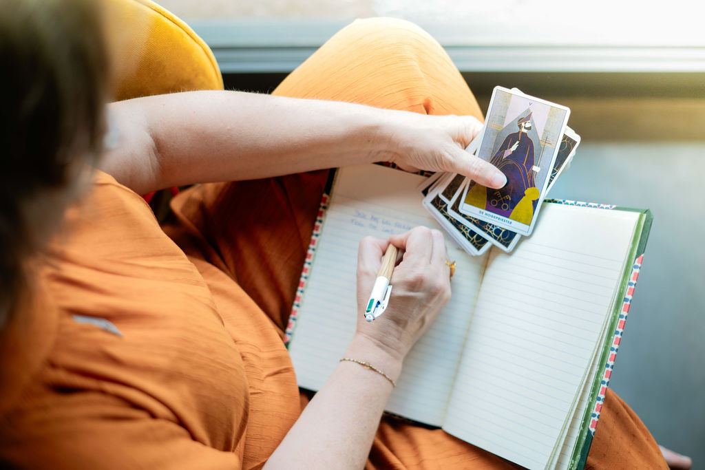 Iemand noteert inzichten in een notitieboek met tarotkaarten in de hand