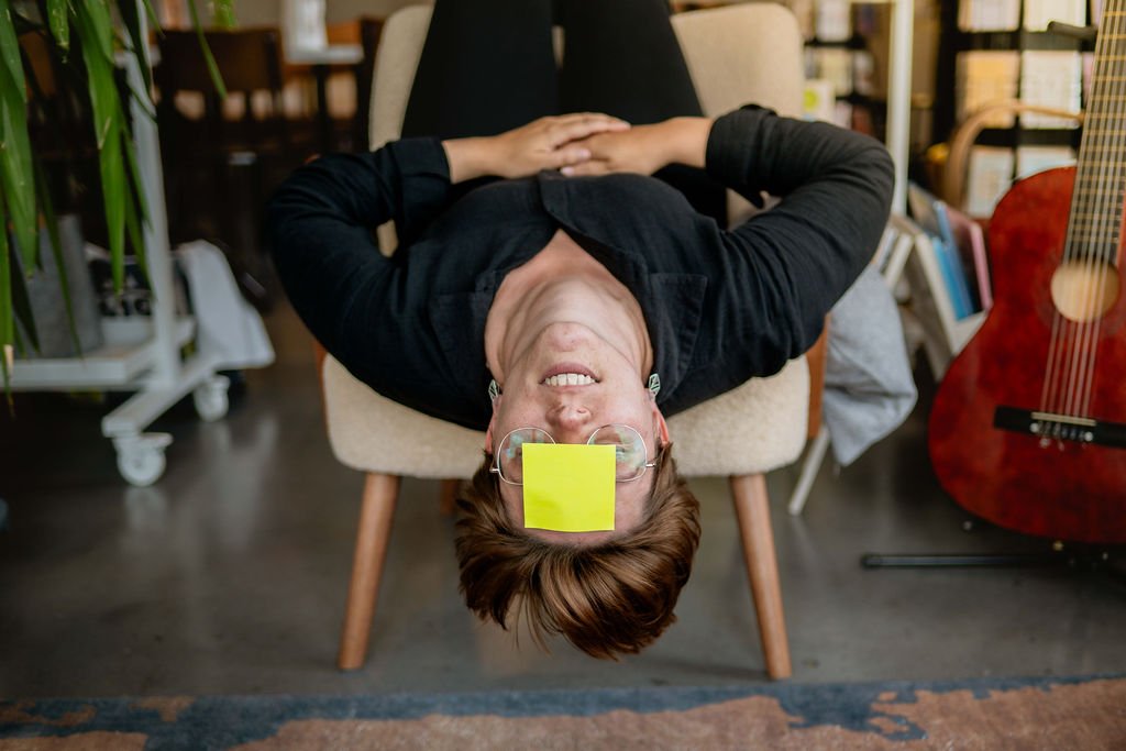 vrouw met post-it op het voorhoofd hangt ondersteboven in de zetel